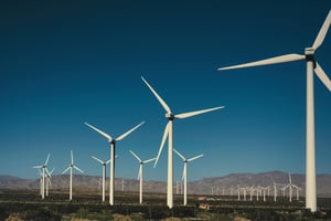 A series of white windmills in a field with a mountainous background in the far distance